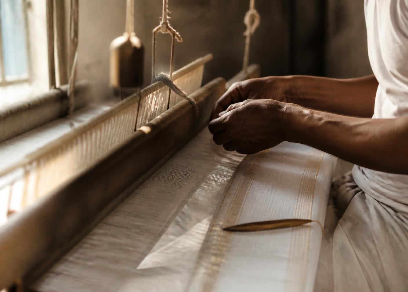 A weaver's hands working fine thread on a wooden pit loom
